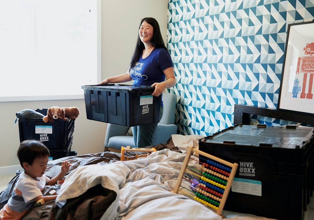 (alt-text: A young mother carries a box from the kid’s playroom as she follows minimalist decluttering tips.) 