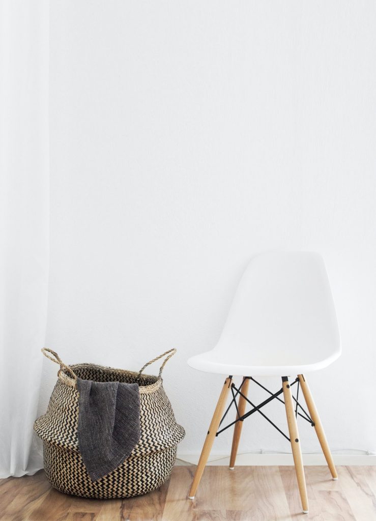 (alt-text: A white chair sits next to a decor basket that stores a blanket as a part of a minimalist home interior.) 