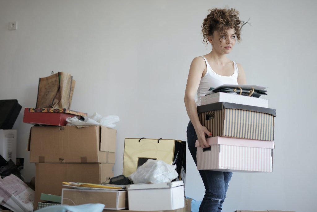 A young woman in a white tank top carries boxes as she figures out how to decide what to throw away when decluttering