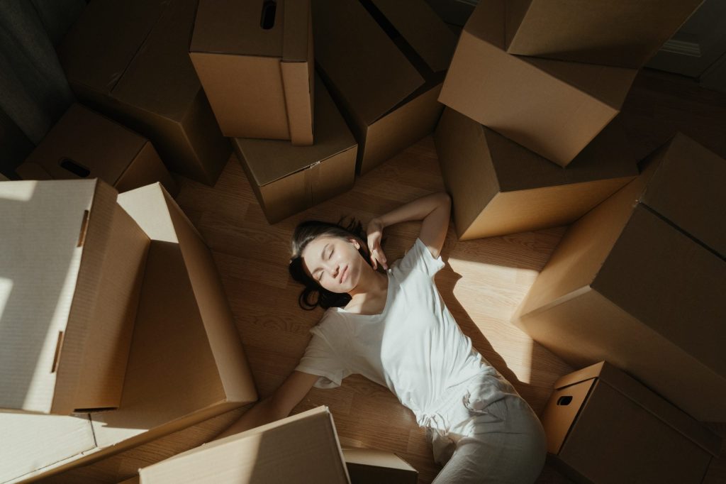 A young woman lays on the floor surrounded by boxes while she tries to declutter her attic.