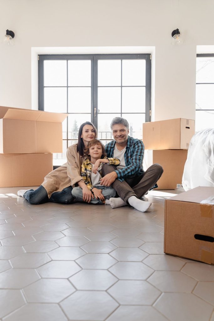 A family sits together in the middle of a room with boxes of clutter after using a declutter schedule to clean their home.