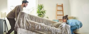 Young Couple Carrying,Sofa While Moving House - Nesta - Nesta couple moving a covered couch in living room